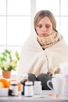 Sick and hopeless. Young woman covered with plaid looking at the medicines while sitting in bed at her apartment photo