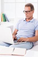 Man working at home. Confident mature man working on laptop while sitting on the couch at home photo