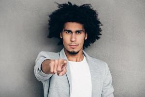 Definitely you Close-up of young African man pointing on you and looking at camera while standing against grey background photo