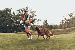 Real joy of being around. Full length of beautiful young woman playing with her dog and smiling while running outdoors photo