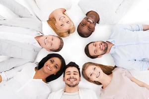 Together we are stronger. Top view of cheerful group of multi-ethnic people laying on their backs and smiling while standing isolated on white photo