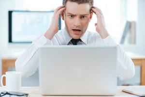 Business troubles. Frustrated businessman working on laptop and touching his head while sitting at his working place photo