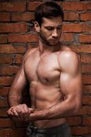 Always in good shape. Confident young muscular man posing while standing against brick wall photo