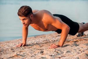 Man doing push-ups. Handsome young muscular man doing push-ups at the riverbank photo