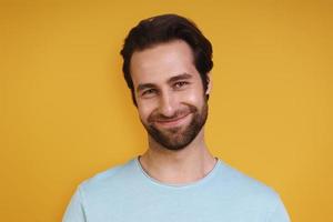 Portrait of young man in casual clothing looking at camera and smiling while standing against yellow background photo