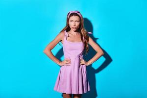 a bad mood. Angry young woman looking at camera and keeping hands on hips while standing against blue background photo