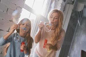 Sharing same hobby. Mother and daughter having fun with soap bubbles while spending time at home photo