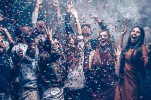 Just having fun. Group of beautiful young people throwing colorful confetti while dancing and looking happy photo