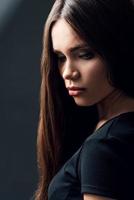 Charming beauty. Attractive young woman with long hair looking down while standing against black background photo
