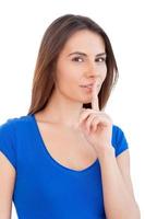 Keep silence Beautiful young woman looking at camera and holding finger on lips while standing isolated on white photo