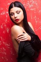 Taking off her clothing. Beautiful young woman taking off her dress and looking away while standing against red background photo