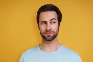 Portrait of young man in casual clothing looking uncertain while standing against yellow background photo