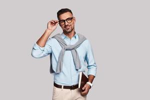 Ready to work. Handsome young man smiling and looking at camera while standing against grey background photo