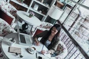 Young and full of ideas. Top view of attractive young smiling woman writing something down while sitting in restaurant photo