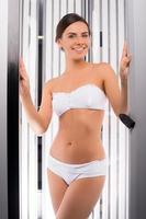 Beautiful woman in solarium. Attractive young woman standing in tanning booth and smiling photo