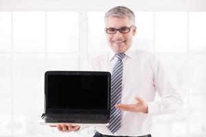 Your text here. Smiling senior man in shirt and tie holding laptop and pointing monitor photo