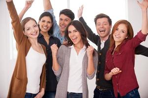 Happy business team. Group of cheerful young people standing close to each other and keeping arms raised photo