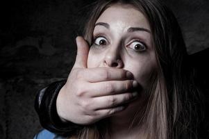 Kidnapping. Terrified young woman with hand covering her mouth staring at camera photo