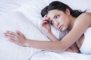 extrañándolo. mujeres jóvenes deprimidas acostadas en la cama y sosteniendo la mano en la almohada foto
