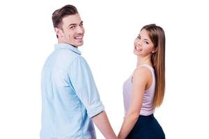 Enjoying their time together. Rear view of beautiful young loving couple looking over shoulder at camera while standing against white background photo