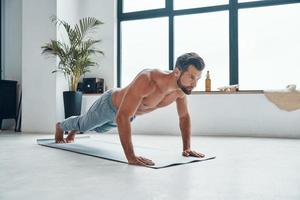 Handsome young man keeping plank position while exercising at home photo