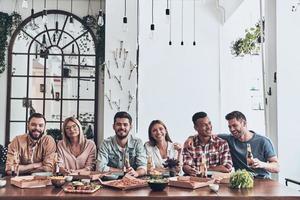 jóvenes tan felices y hermosos con ropa informal sonriendo mientras cenan en el interior foto