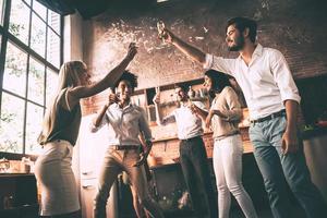 anima a los amigos vista en ángulo bajo de jóvenes alegres bailando y bebiendo mientras disfrutan de una fiesta en casa en la cocina foto