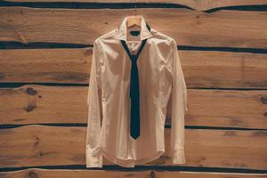 Cothes on the wall. White shirt and tie hanging on the rough wooden wall photo