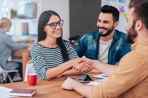 Welcome on board Confident young woman and man shaking hands and smiling while sitting at the desk in office photo