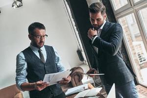 Analyzing sales. Two young modern men in formalwear working together while sitting indoors photo