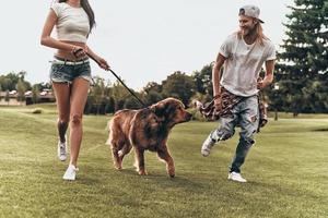 Young modern couple playing with their dog while running in the park photo