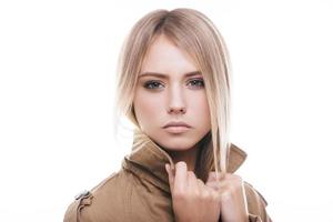 Autumn fashion. Attractive young woman in coat adjusting her collar and looking at camera while standing against white background photo
