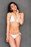 Fit beauty. Beautiful young mixed race woman in white bikini posing against grey background and looking at camera photo