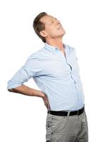 Feeling pain in back. Frustrated mature man touching his back and expressing negativity while standing against white background photo