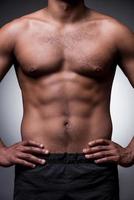 Perfect male body. Close-up of shirtless African man holding hands on hip while standing against grey background photo