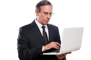 empresario en el trabajo. hombre maduro confiado en ropa formal que trabaja en la computadora portátil mientras está de pie aislado sobre fondo blanco foto