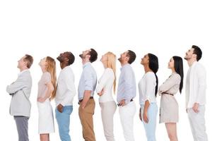 What is that Side view of positive diverse group of people in smart casual wear looking up while standing in a row and against white background photo