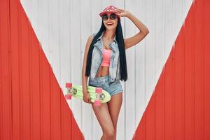 Queen of skate park. Happy young women holding skateboard and smiling while standing outdoors photo