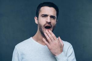 Feeling bored. Handsome young man yawning and looking bored while standing against grey background photo