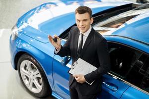 Let me assist you in your vehicle search. Top view of handsome young classic car salesman standing at the dealership holding a key photo