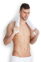 Man wrapped in towel. Cheerful young muscular man wrapped in towel looking at camera while standing isolated on white background photo