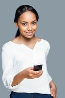 Beauty with mobile phone. Beautiful young African woman holding mobile phone and looking at camera smile while standing against grey background photo