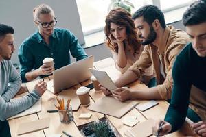 Thinking in one direction. Top view of young modern people in smart casual wear using modern technologies while working in the creative office photo