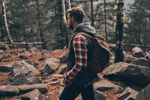 Young man carrying backpack and looking away while standing in the woods photo