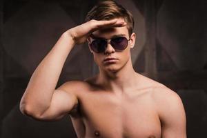 Confident and handsome. Handsome young man wearing sunglasses and holding hand on forehead while standing against metal background photo