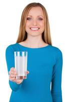 Take aspirin Young woman holding a glass with water and aspirin in it while standing isolated on white photo