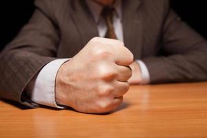 My word is law Close-up of man in formalwear holding fist on the table and isolated on black photo