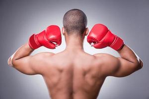 simplemente lo mejor. vista trasera del hombre africano sin camisa en guantes de boxeo de pie contra el fondo gris foto