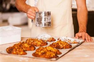 Making croissants perfect. Close-up of baker in apron adding sugar to the pastry photo