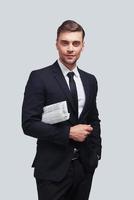 Confident business expert. Good looking young man in full suit smiling and looking at camera while standing against grey background photo